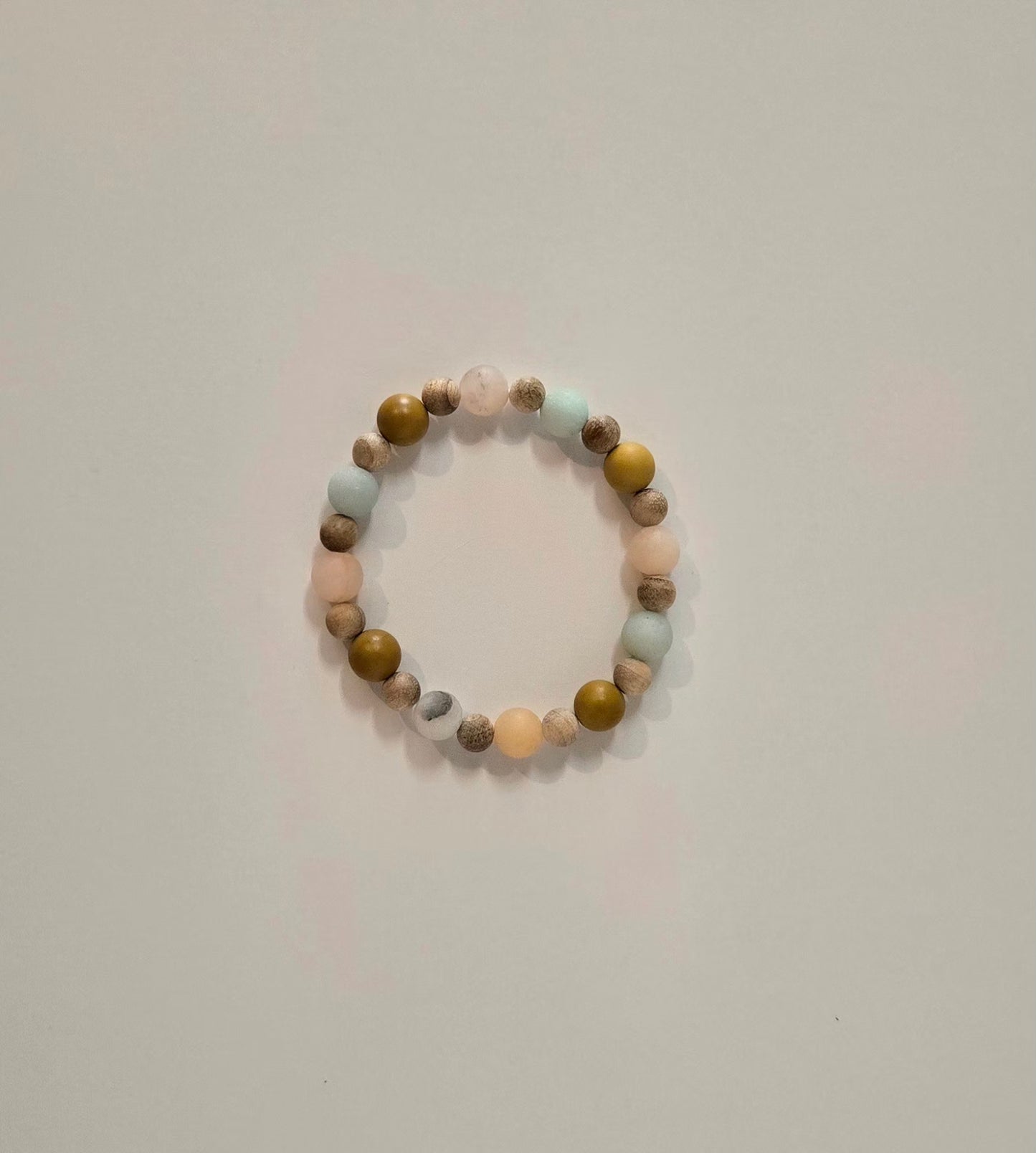 A beaded stretch bracelet with alternating matte pastel pink, light blue, olive green, and brown marbled beads, photographed on a plain light gray background.