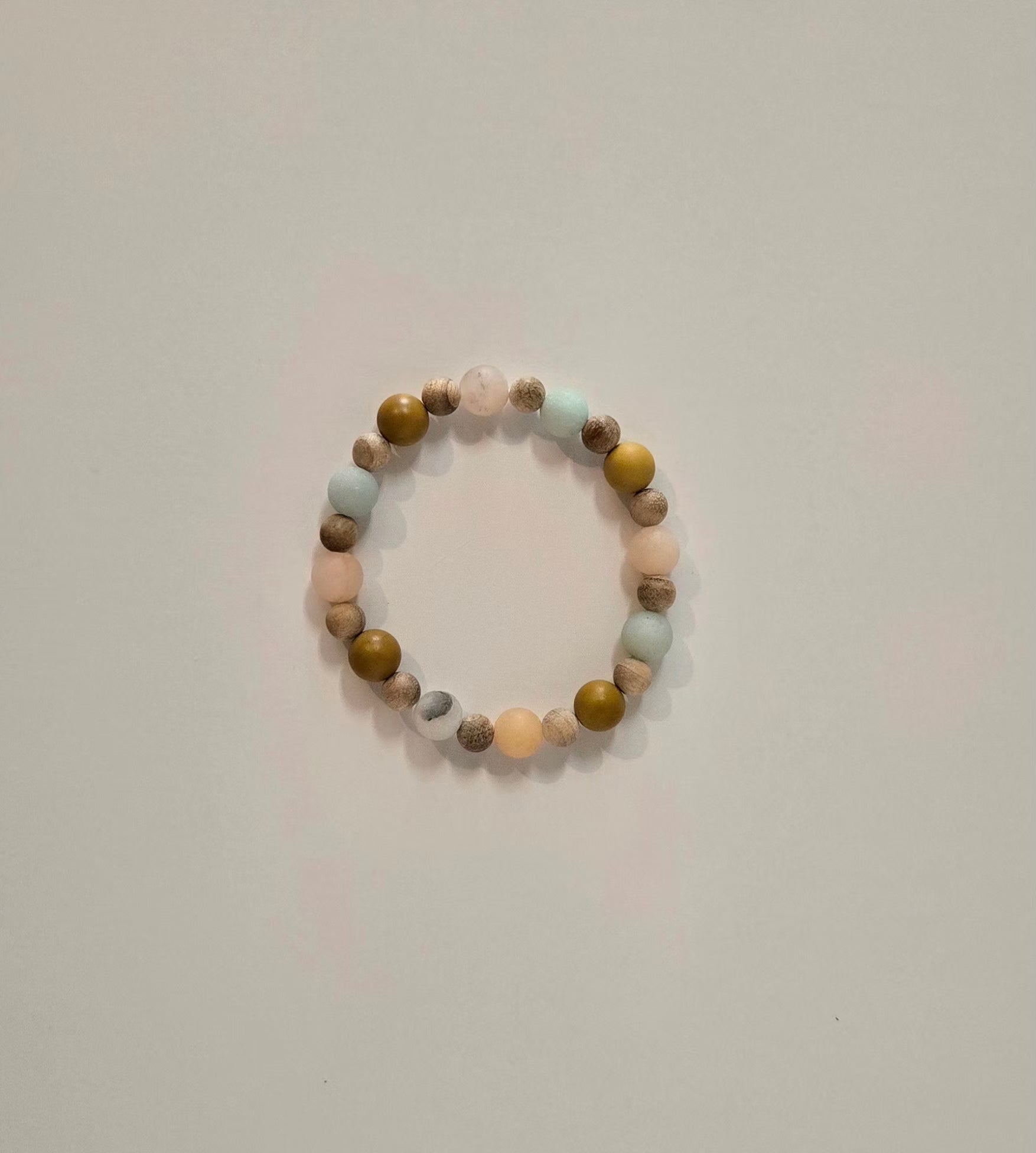A beaded stretch bracelet with alternating matte pastel pink, light blue, olive green, and brown marbled beads, photographed on a plain light gray background.