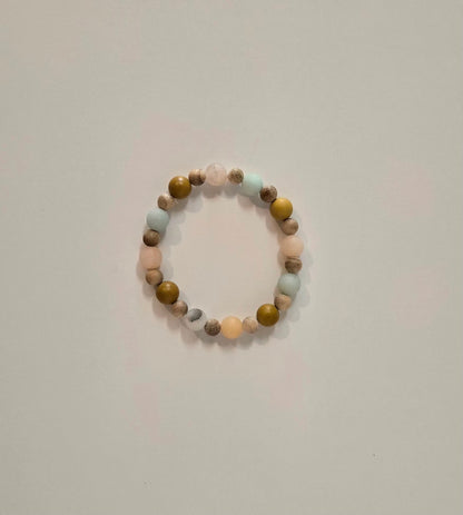 A beaded stretch bracelet with alternating matte pastel pink, light blue, olive green, and brown marbled beads, photographed on a plain light gray background.
