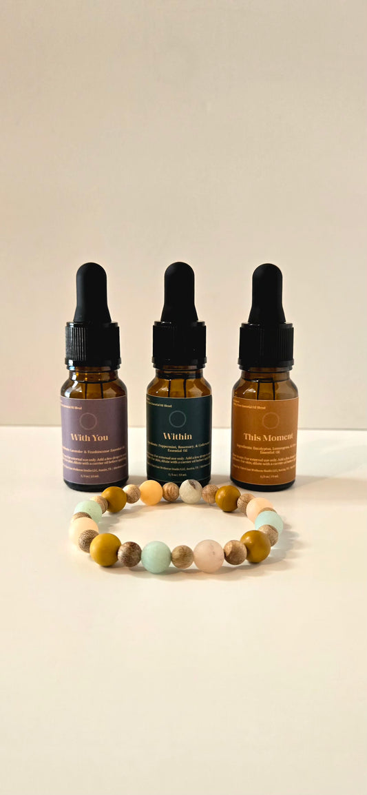 Three amber glass dropper bottles with black caps and labels reading behind a round beaded bracelet on a plain light beige background.