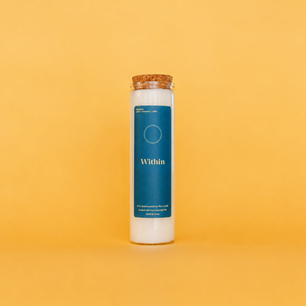 A tall white soy wax candle in a clear glass jar with a cork stopper, featuring a dark teal label that reads 'Within' on a solid yellow background.