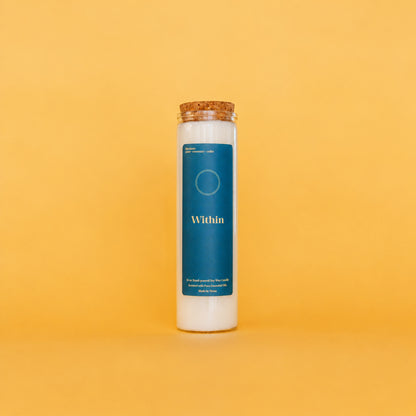 A tall white soy wax candle in a clear glass jar with a cork stopper, featuring a dark teal label that reads 'Within' on a solid yellow background.